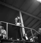 Gymnastikuppvisningen, 25/5 1941. 
En man i mörk kostym talar i en mikrofon, på läktaren till Värendsvallen.