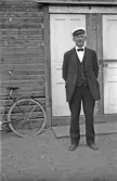 Man i kostym och studentmössa utanför trähus, 1920-tal