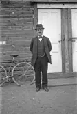 Man i kostym och hatt framför trähus, 1920-tal