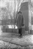 Kvinna i hatt och varm kappa vid minnessten, 1920-tal