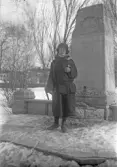 Kvinna i hatt och kort kappa med boa vid minnessten, 1920-tal