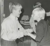 Elever från Brattåsskolans åk 6 är på lägerskola till Ransbergs Herrgård i Värmland cirka 1965 - 1975. Två elever dansar och har kul tillsammans under en kvällsaktivitet (fritid). I bakgrunden skymtar en rullbandspelare som står på ett bord.