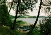 En båt ligger förtöjd vid en brygga i Rådasjön, Mölndal, år 1994. I bakgrunden Slottsviken.