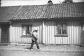 En man promenerar på trottoaren förbi ett envånings timrat trähus på Norrgatan i Varberg. Fotograf okänd.