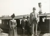 Ett sällskap med tre män och en kvinna med hatt framför en ångslup, Gysinge omkring 1900.