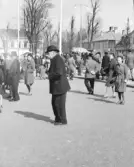 Miljöbild från Varbergs torg med en äldre man i fokus. Han och flera andra verkar betrakta något som händer till vänster ur bild. I bakgrunden en folksamling och till höger ses kv Apoteket.