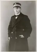 Nyblivne kronolänsmannen Ernst Bjersing, ca 1917, i länsmansuniform med rock och skärmmössa och med en portfölj under armen.
Knäbild, halvprofil. Ateljéfoto.