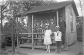 Finklädd grupp på verandan till sin kolonistuga, 1920-tal
