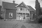 Familj vid hus med veranda med vacker snickarglädje, 1920-tal