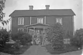 Familj med trädgårdsredskap framför hus, 1920-tal