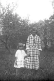 Kvinna i rutig klänning med liten flicka klädd i vit klänning och rosett i håret, 1920-tal