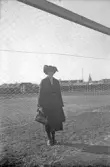 Kvinna iförd kappa, hatt och handväska stående i fotbollsmål, 1920-tal