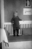 Barn i stickad dräkt stående i kökssoffa, 1920-tal