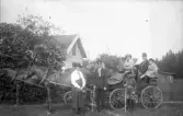 Två hästar med vagn och passagerare medan tre personer står framför dessa, 1920-tal