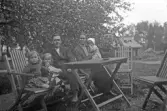 Familj med tre små barn sittande i trädgårdssoffa, 1920-tal