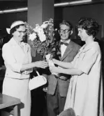 Kontorsbiträdet fru Ulla Johansson överlämnar blommor till fru Inga
Malmrén, vid besöket på girobok-föringen, avdelning E, där herr
Malmréns konto föres. Fru Johansson var för dagen bordschef vid
bokföringsbord 90.