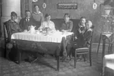 Familj sitter runt bord dukat för kaffe, bullar och kakor, 1920-tal