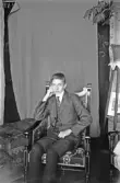 Ung man sitter i en stol framför ett övertäckt draperi, 1920-tal