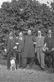 Fem män i kostym och uniform med hund samlade i en park, 1920-tal