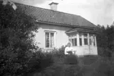 Äldre kvinna utanför stuga, 1920-tal