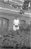 Kvinna i plantering framför hus, 1920-tal