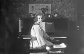 Kvinna vänder sig mot kameran från pianot som hon spelat på, 1920-tal