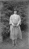 Kvinna med randig klänning med hatt och handväska i trädgård, 1920-tal