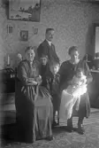Ett litet barn i dopklänning i moderns knä med familjen runt sig, 1920-tal