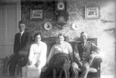 Leende familj fotograferas sittande i finsoffan, 1920-tal