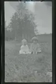 Två små barn sitter i gräset utomhus.