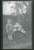 Porträtt av ett par syskon, det minsta sitter i en barnvagn.