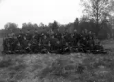 Foto av en pluton meniga i uniform, som samlats för gruppfotografering på en äng.