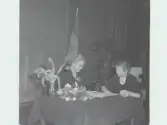 Karin Sandklef och Karin Olsson sitter vid ett bord under Rädda Barnens 10-årsjubileum, Artikel i samband med bilden publicerad i Varbergs Tidning 1954-03-05.
