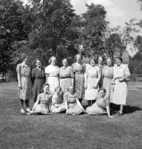 Ett antal kvinnor i olika åldrar har ställt upp sig för fotografen på en gräsmatta. 
I bakgrunden skymtar ett bostadshus.