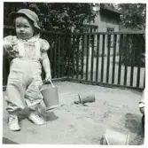 Bild på ett barn som leker med hink och spade i sandlådan, sommaren 1958.