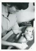 Fotografi på en barnsköterska som sköter om och  badar en baby, 1963.