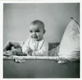 Fotografi på Per 8 1/2 månader, sittande i en liten säng.