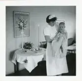 Fotografi på ett dop av Michel på Lilla Källbäck med barnsköterska som håller honom, 1959.