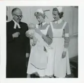 Foto på dopdag för Nils-Åke med pastor Bäckström, barnsköterskan Margit Forsell som håller i gossen samt en till barnsköterska.