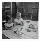 Fotografi på Susanna och Peter som ligger på golvet på en filt med leksaker framför sig i Lilla Källbäck.