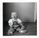 Fotografi på Mikael med hängselbyxor sittande på golvet.