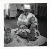 Fotografi på Marina, Mikael, Frank och Stig samt en barnsköterska som har två i famnen, på en filt i Lilla Källbäck.