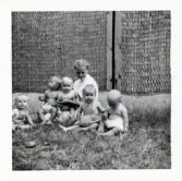 Fotografi på Mikael, Eva, Bedde, Bent-Åke, Marita med barnsköterskan Kerstin Hjelm sittande i gräset i Lilla Källbäck.