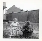 Fotografi på Majvor sittande i en liten barnstol en sommardag i Lilla Källbäck.