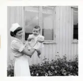 Fotografi på en barnsköterska som håller upp lilla Elionore framför Lilla Källbäck.