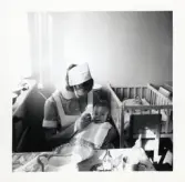 Fotografi på en barnsköterska som matar lilla Birthe i Lilla Källbäck.