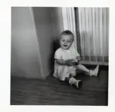 Fotografi på en glad liten Birthe sittande på golvet med leksak i handen i Lilla Källbäck.