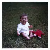 Fotografi på Alexander som sitter i gräset med en nalle bredvid sig.