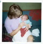 Fotografi på en bebis i famnen på en kvinna som sitter i en soffa.