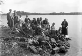 Foto av ett antal damer på utflykt. De har slagit sig ner vid en stenig sjöstrand i närheten av Bergsnäs.